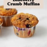 Vegan blueberry crumb muffins are resting on a white surface against a white tile backdrop.