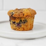 A vegan blueberry crumb muffin rests on a round, rimmed white plate.