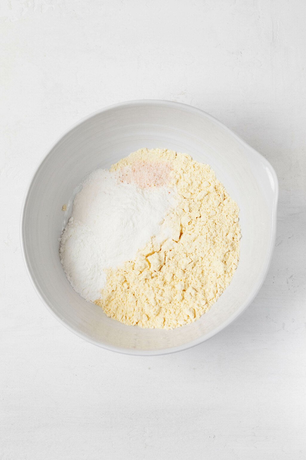 A pale yellow flour and other dry ingredients are being whisked in a mixing bowl.