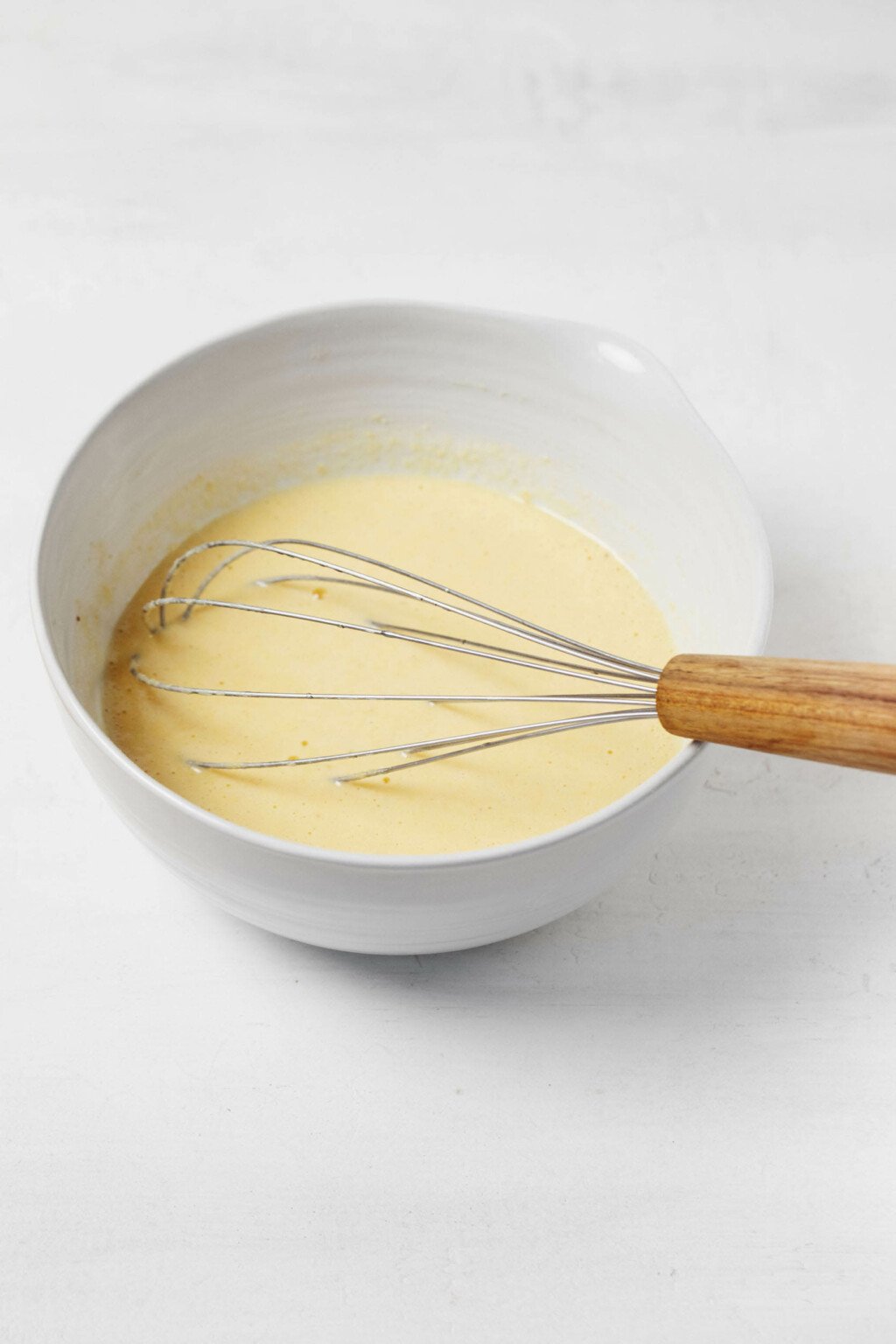 A white mixing bowl holds a pale yellow colored batter.