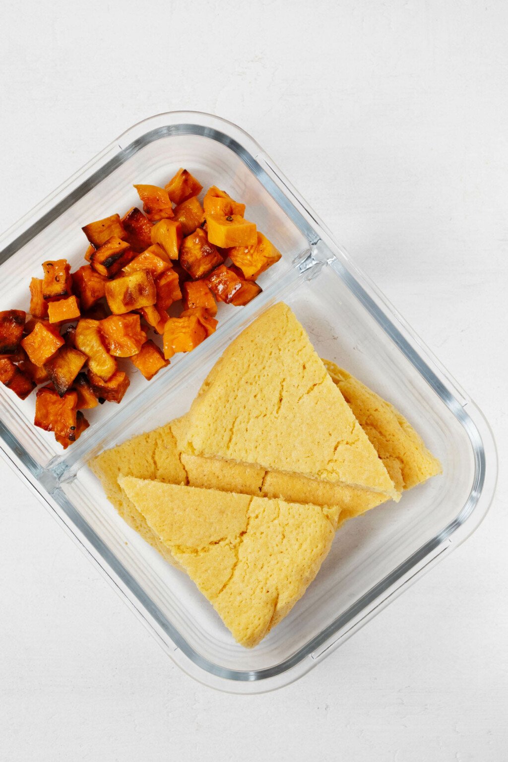 Slices of a vegan chickpea frittata have been packed in a glass container with roasted sweet potato cubes.