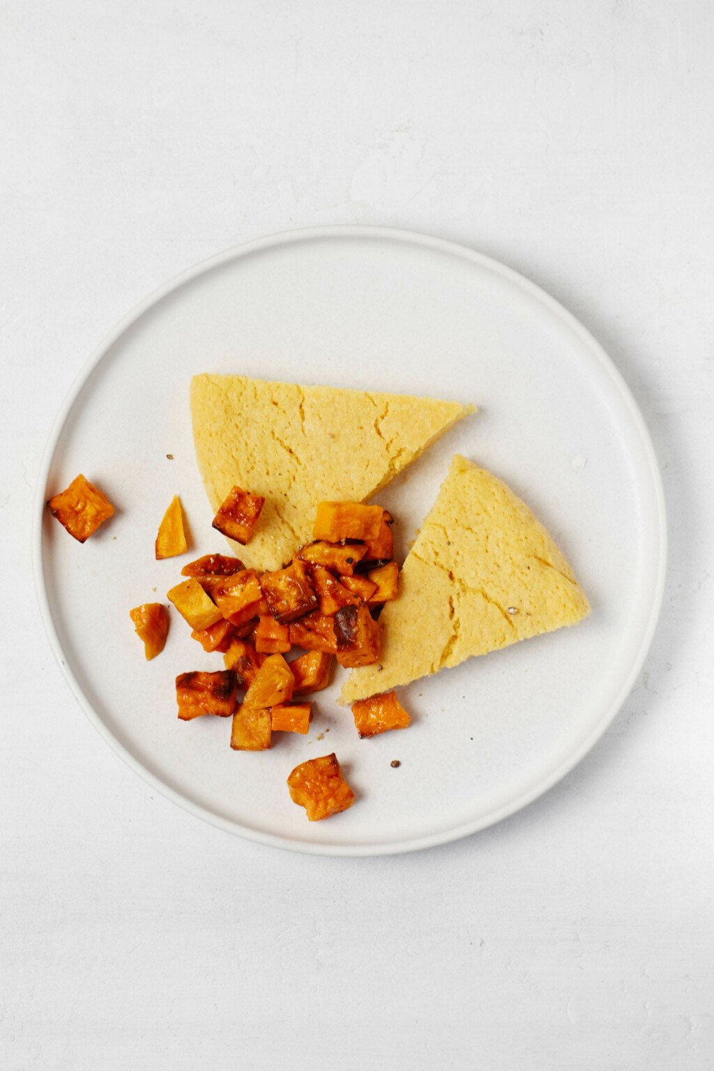 Slices of a vegan chickpea frittata are accompanied by roasted sweet potato cubes on a round plate.