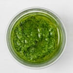 An overhead image of a small, glass jar, which is filled with bright green pesto.