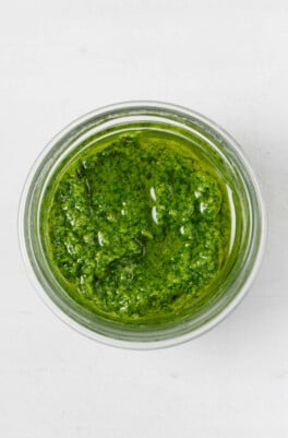 An overhead image of a small, glass jar, which is filled with bright green pesto.