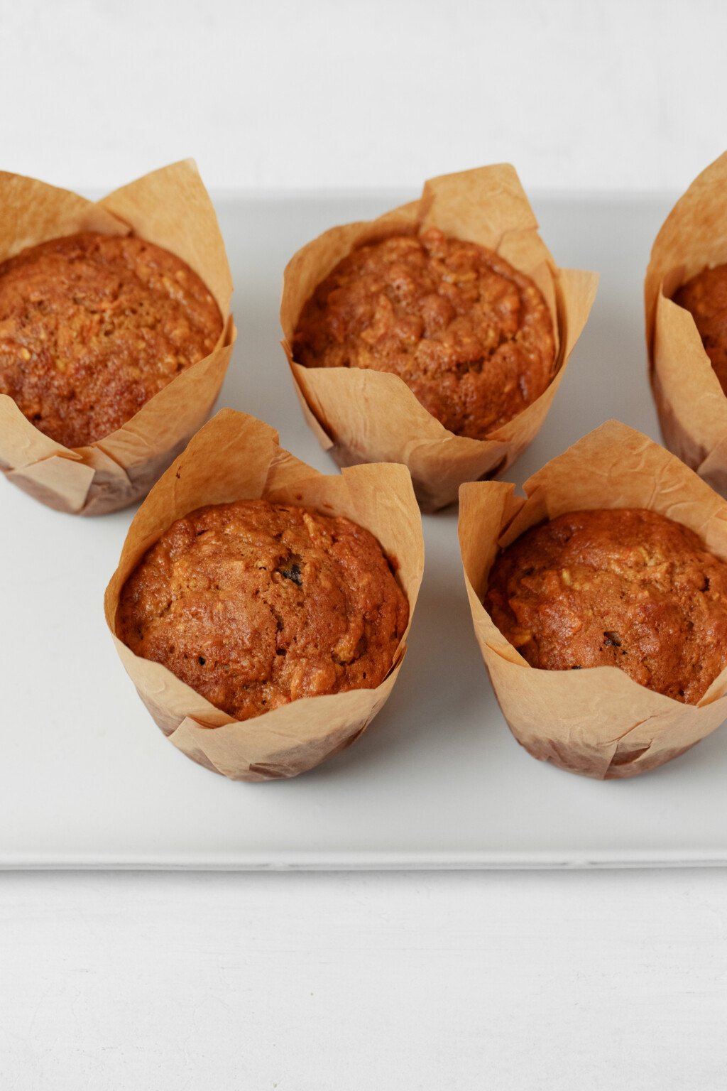 A white platter has been lined with golden brown, vegan morning glory muffins.