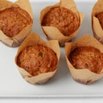 A white platter has been lined with golden brown, vegan morning glory muffins.