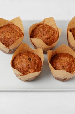 A white platter has been lined with golden brown, vegan morning glory muffins.