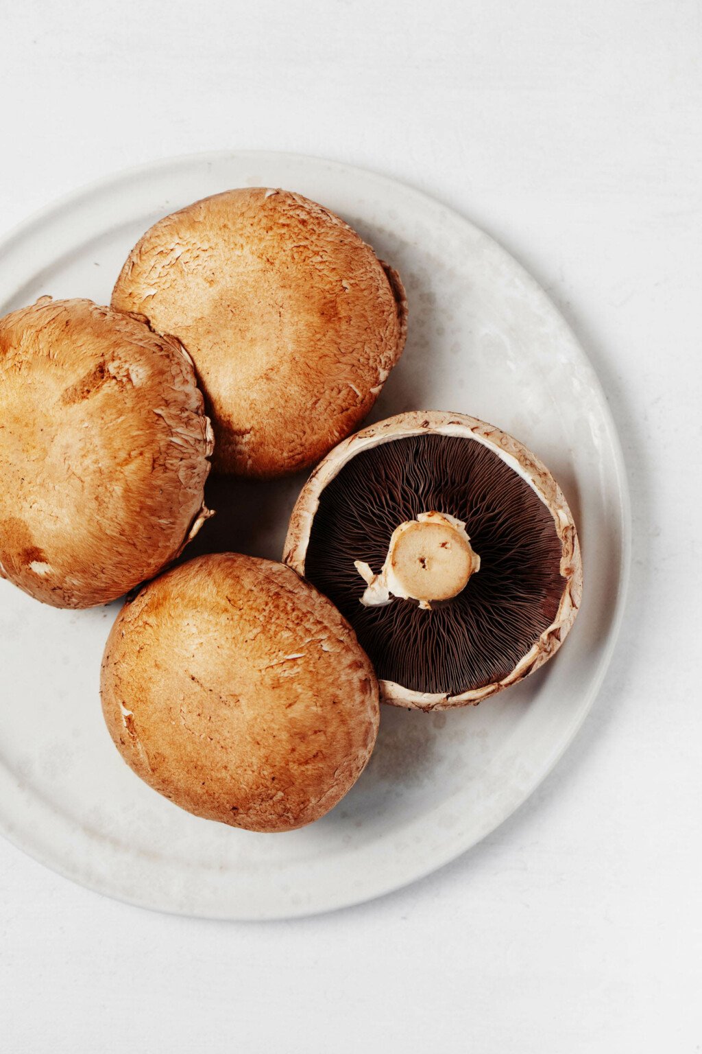 A round, white plate is covered in four brown, portobello mushroom caps.