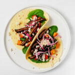 An overhead image of two neatly folded vegan portobello mushroom tacos, which are garnished with thinly sliced pickled red onion and plant-based 