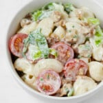 A round, white bowl is filled with a vegan BLT-inspired pasta salad, made with creamy dressing, cherry tomatoes, and chopped greens.