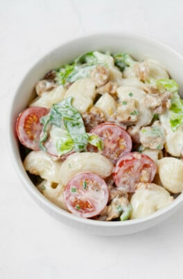 A round, white bowl is filled with a vegan BLT-inspired pasta salad, made with creamy dressing, cherry tomatoes, and chopped greens.