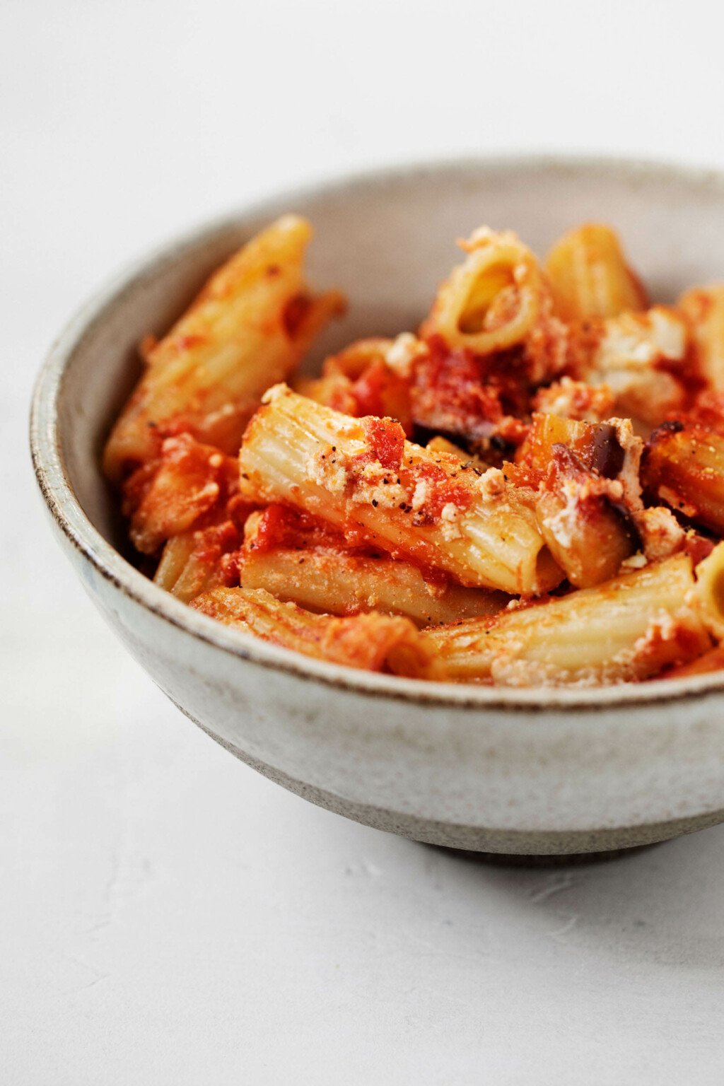 A round, white gray ceramic bowl is filled with a baked rigatoni pasta.