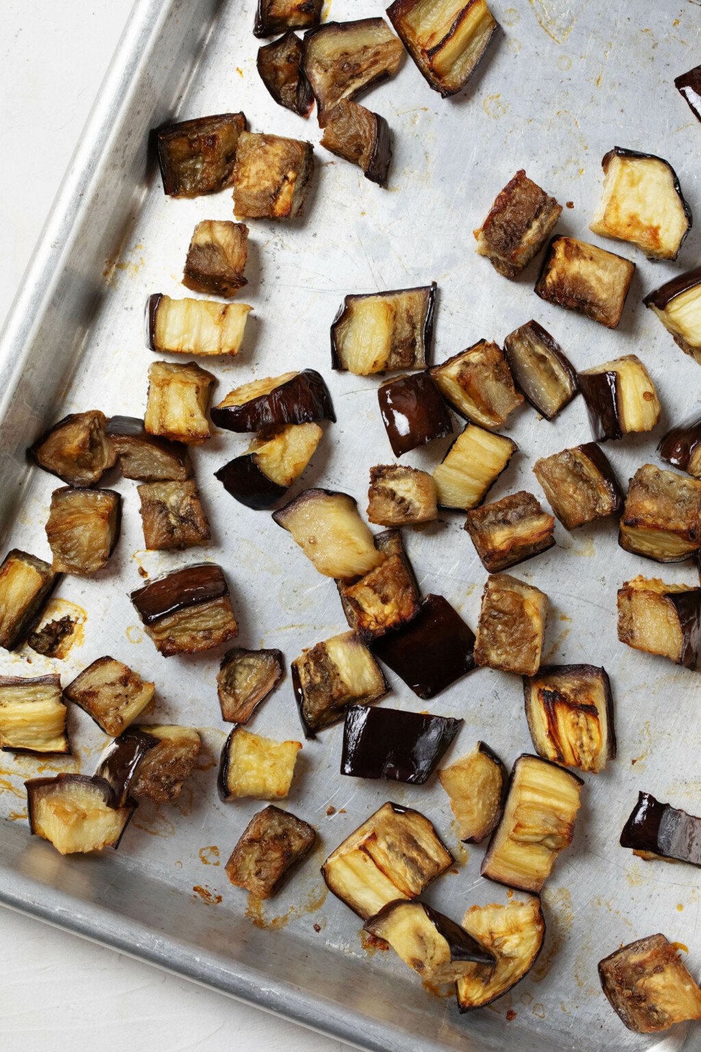 A baking sheet is pictured with tender, browning roasted eggplant cubes on top.