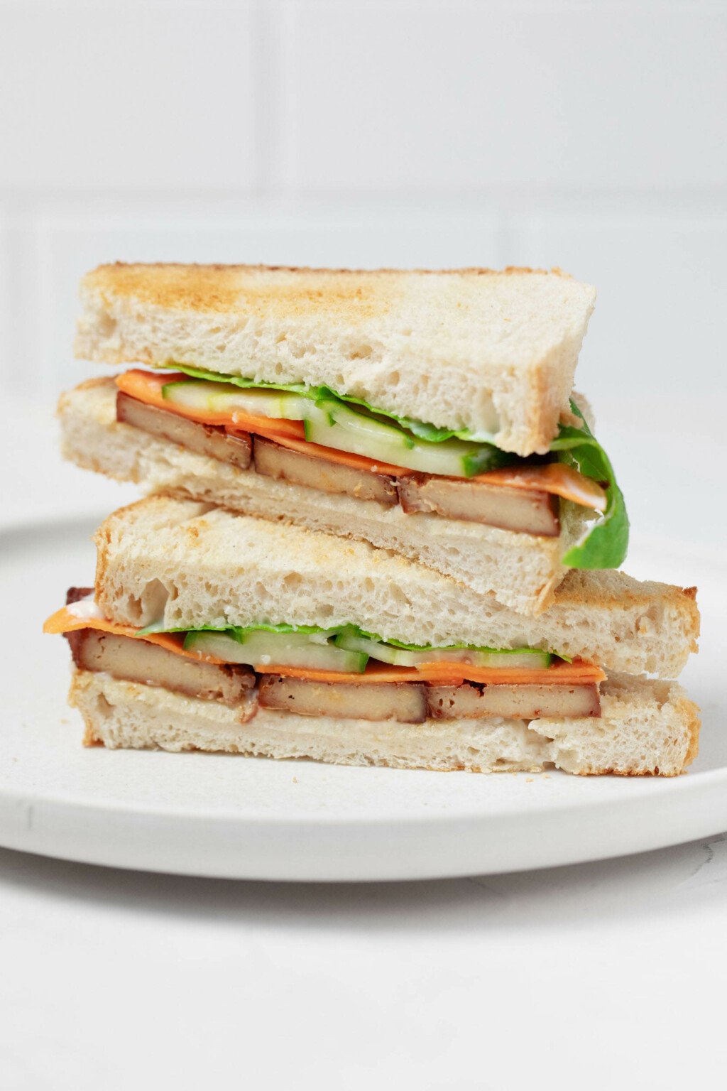 Μια γωνιακή εικόνα ενός σάντουιτς τουρσί λαχανικών και καπνιστού τόφου.  Το σάντουιτς έχει κοπεί στη μέση, αποκαλύπτοντας μια διατομή με αγγούρι, καρότο και μαγιονέζα, μαζί με το τόφου. 