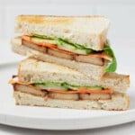 An angled image of a pickled vegetable and smoky tofu sandwich. The sandwich has been cut in half, revealing a cross section with cucumber, carrot, and mayonnaise, along with the tofu.