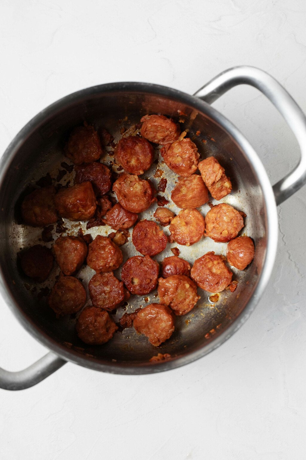 Round slices of sausage are being browned in a large soup pot.