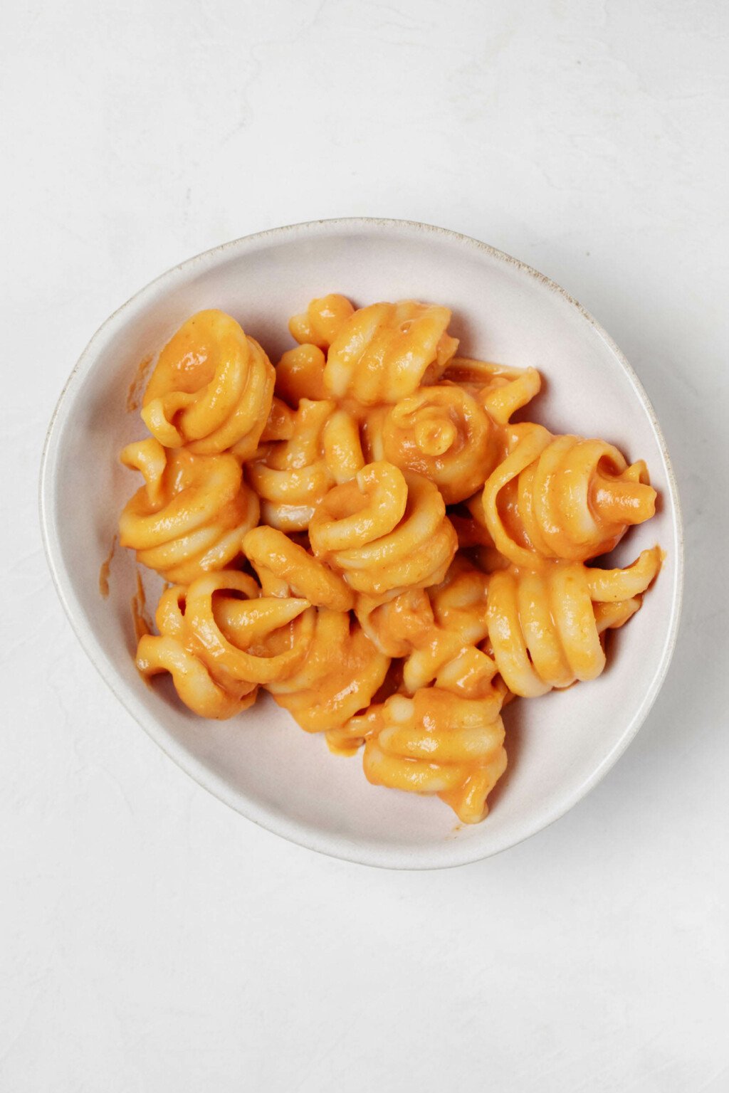 An overhead image of a small, asymmetrical white bowl, which is filled with a vegan pumpkin pasta.