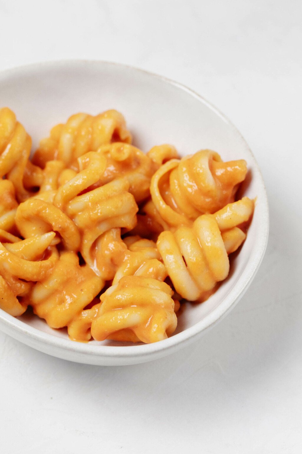 A close up image of a bowl with corkscrew shaped pasta and a creamy, orange, pumpkin-based sauce.