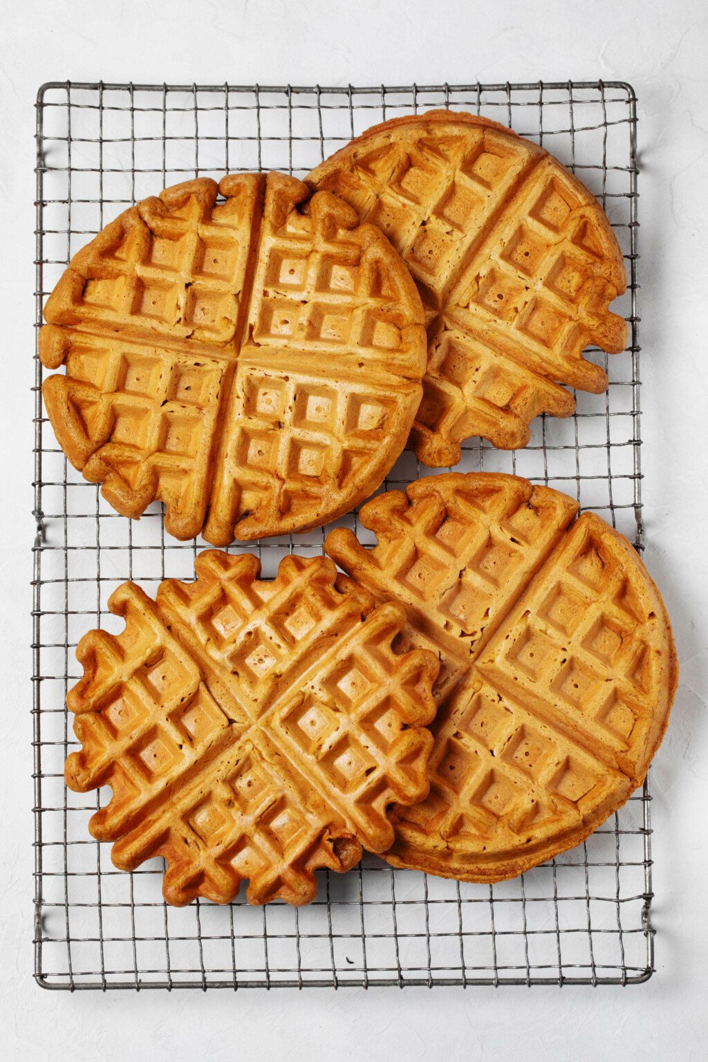 A wire cooling rack is holding golden brown, slightly orange-hued Belgian waffles.