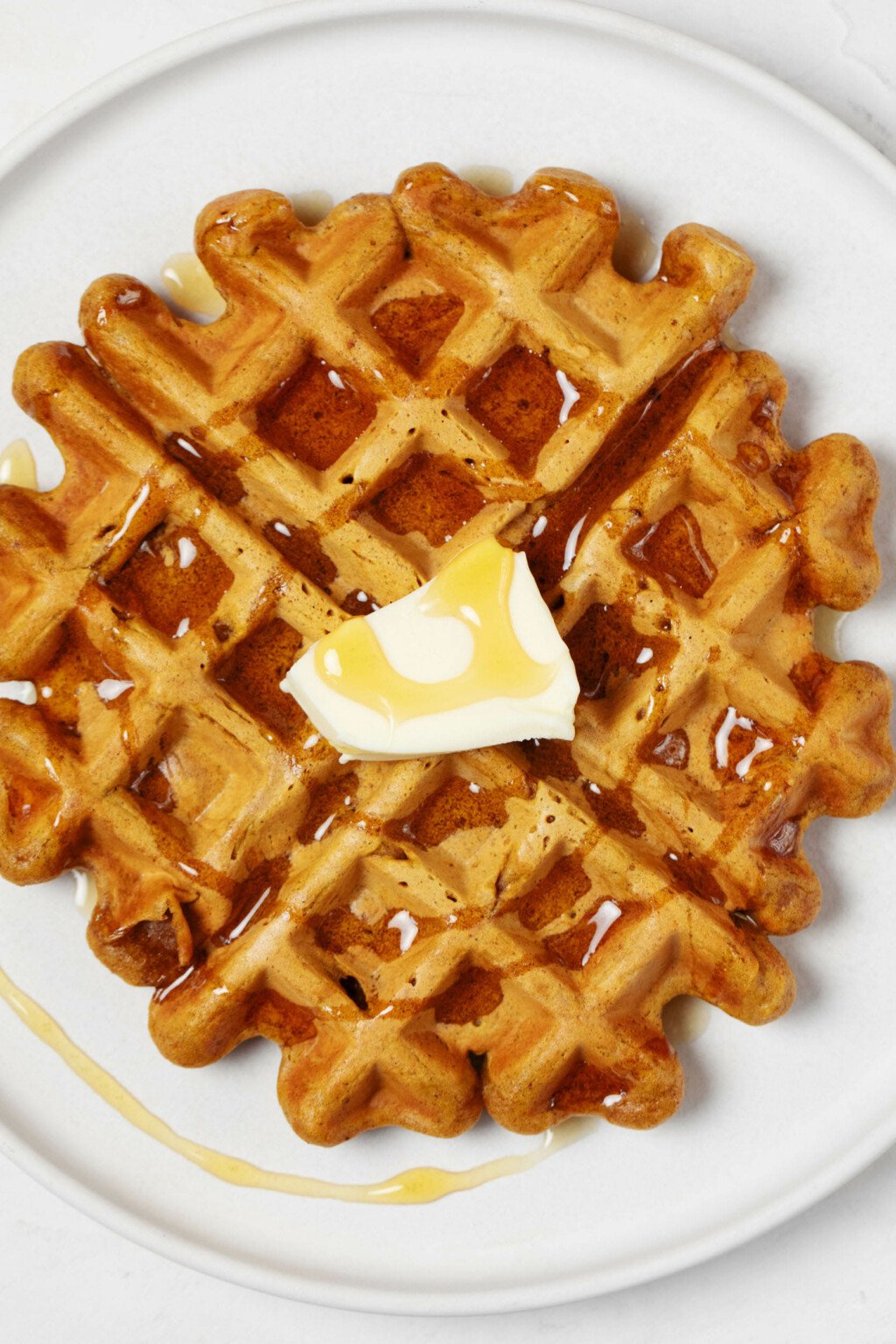 A zoomed-in, overhead image of a deeply golden colored waffle. The waffle is topped with a little pat of butter and some syrup.