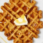 A zoomed-in, overhead image of a deeply golden colored waffle. The waffle is topped with a little pat of butter and some syrup.