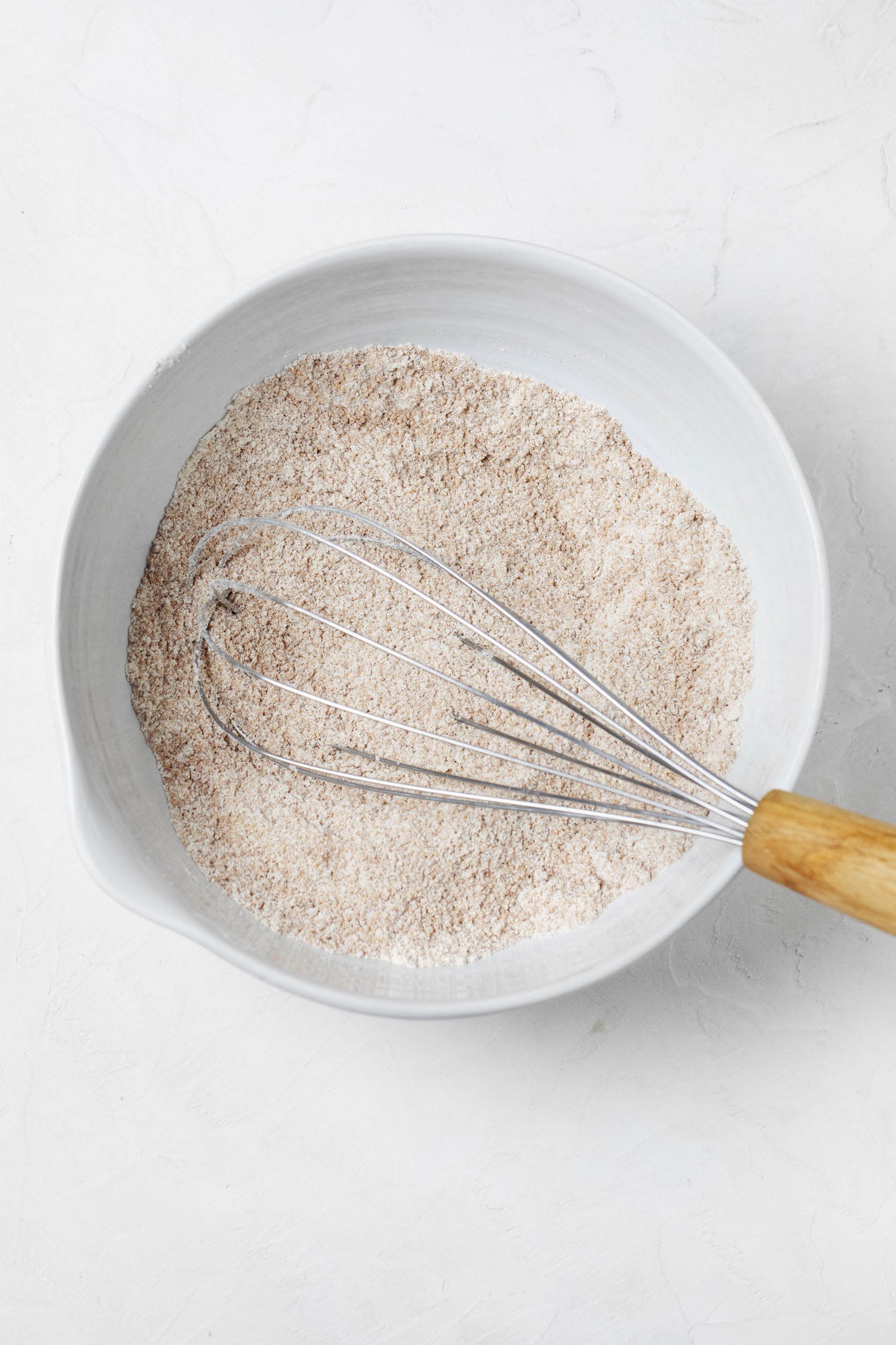 Dry ingredients, including all-purpose flour, cinnamon, and sugar, are pictured overhead in a white mixing bowl.