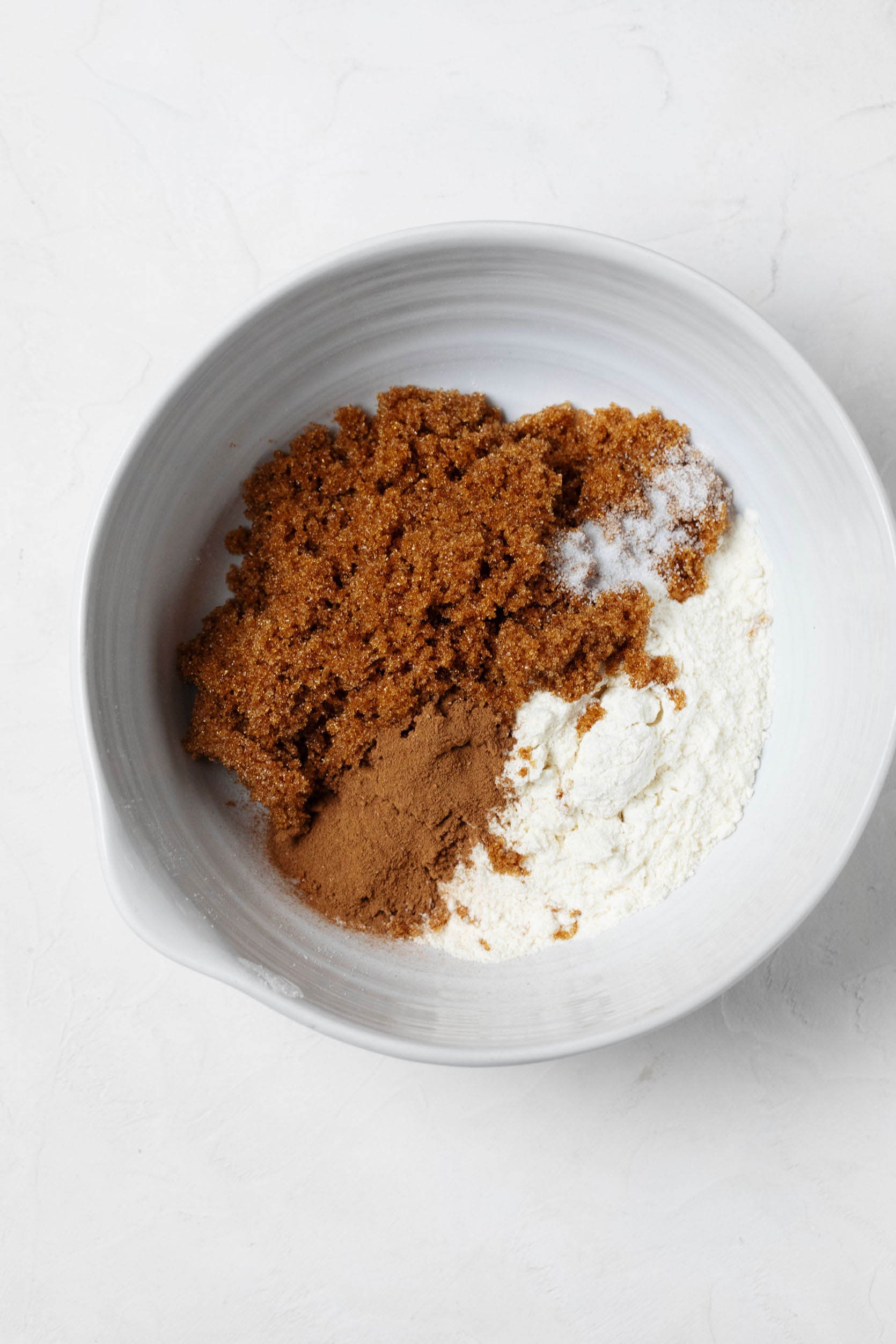 Dry ingredients, including all-purpose flour, cinnamon, and sugar, are pictured overhead in a white mixing bowl.