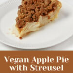 A hearty slice of vegan apple pie with streusel topping has been arranged on a small, round white plate.