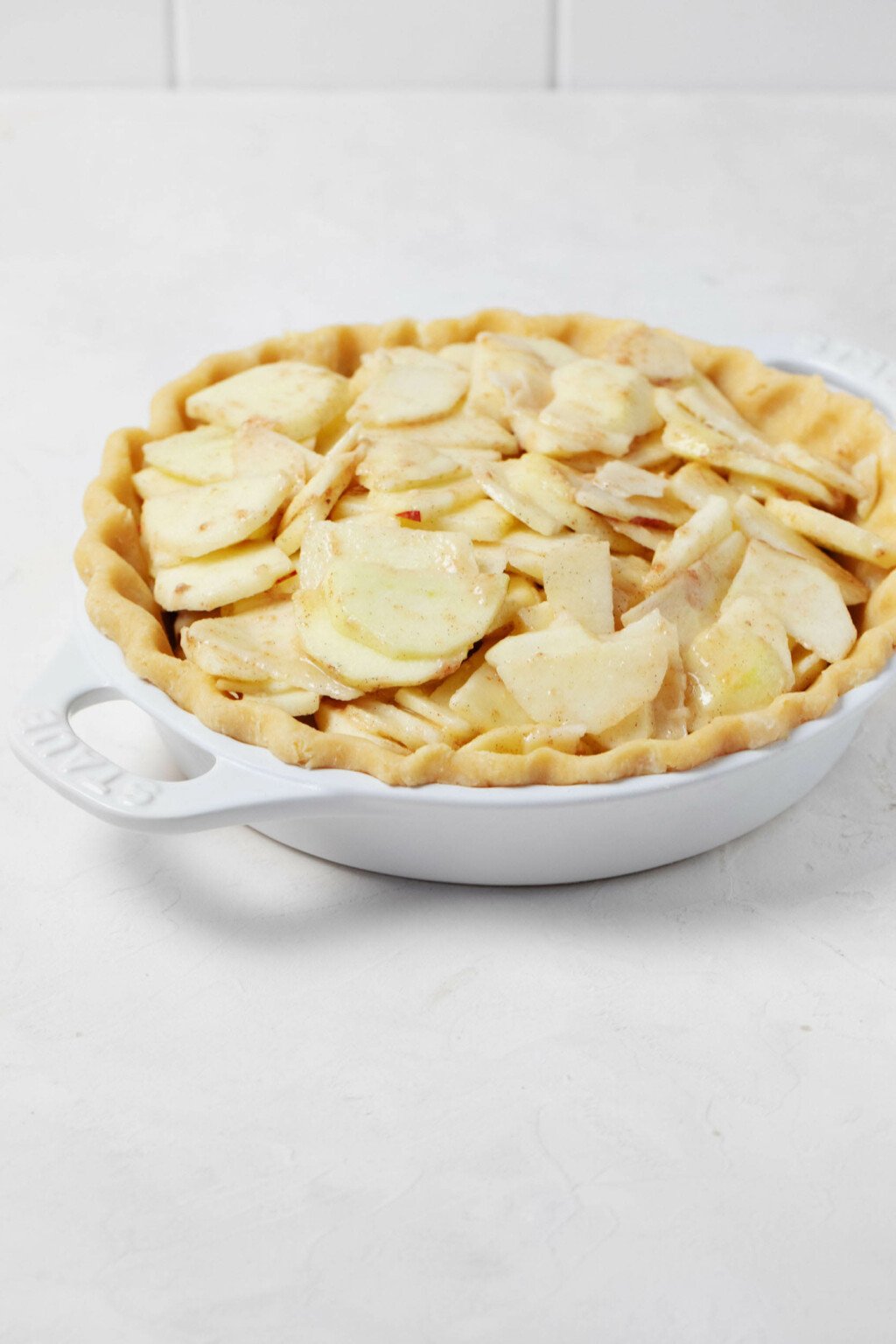 An angled image of a white pie plate, which has been filled with thinly sliced, glazed apples.