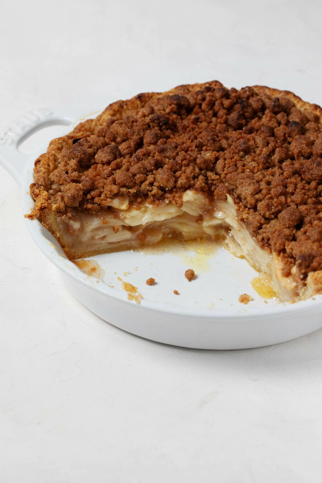 An angled image of a vegan apple crumb pie, which has a couple slices missing from the pie dish.