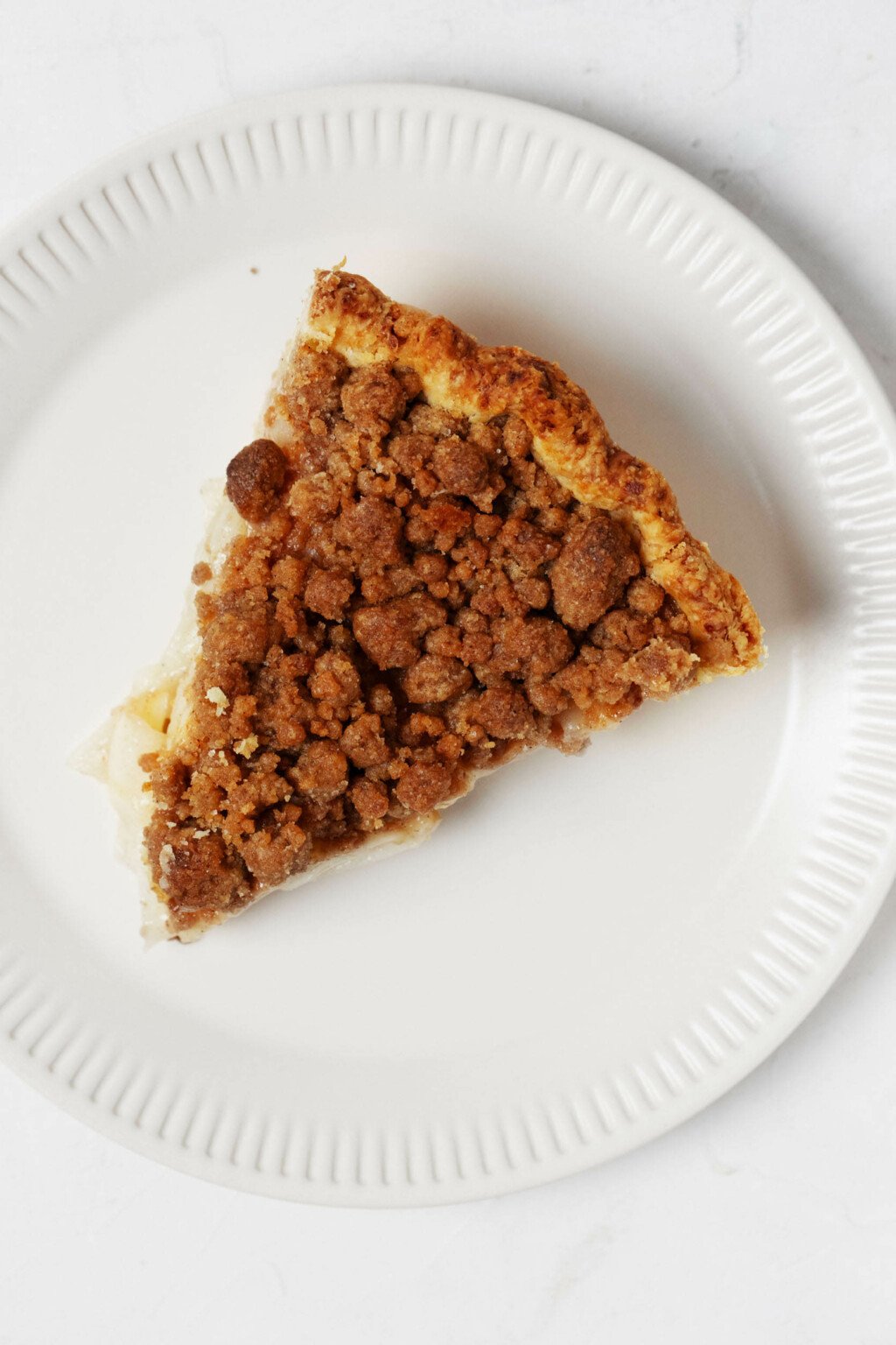 An overhead image of a slice of vegan crumb pie, which is plated on a small, white ceramic plate.
