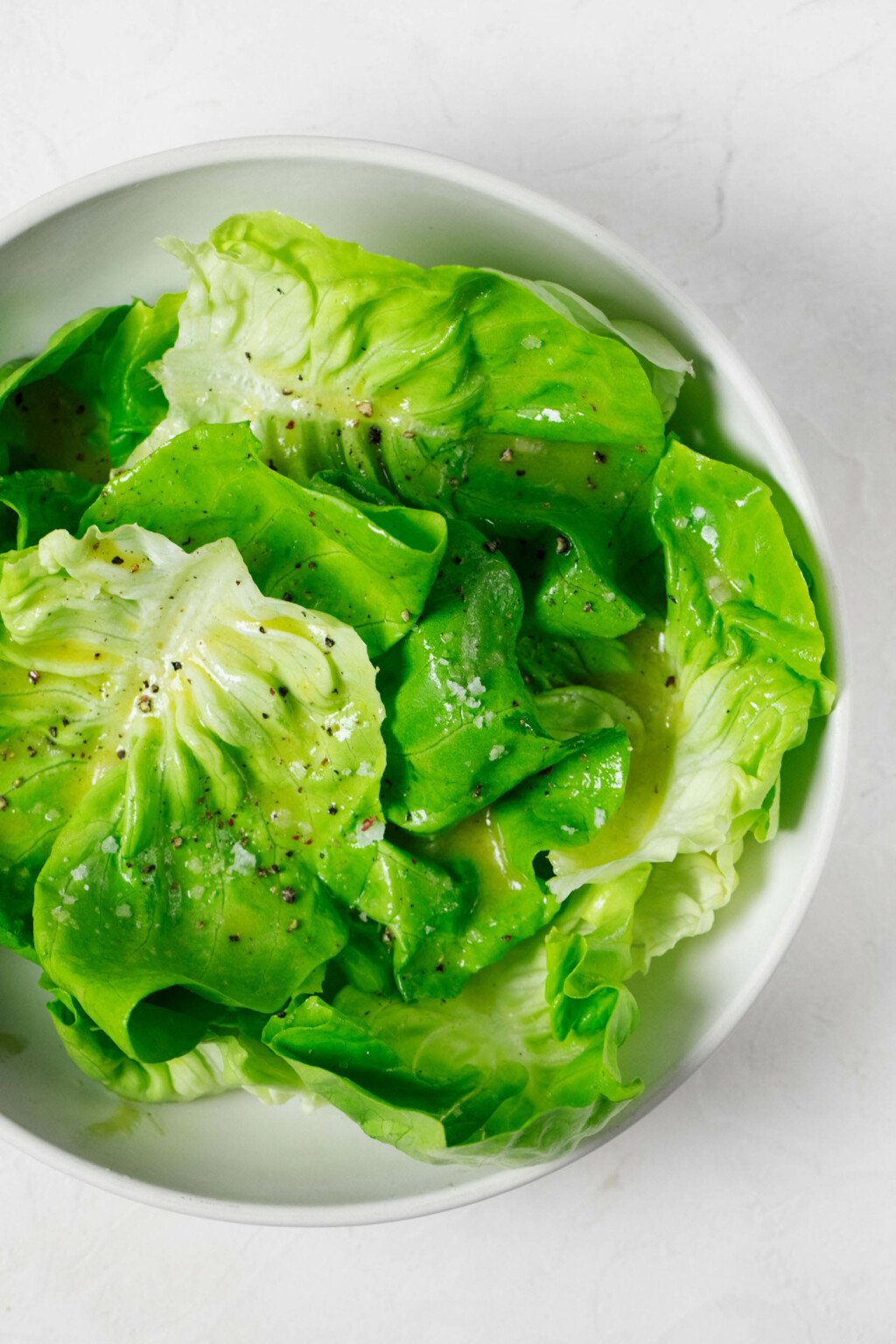 An overhead, close-up image of butter lettuce leaves, which have been mixed with a simple Champagne vinaigrette.