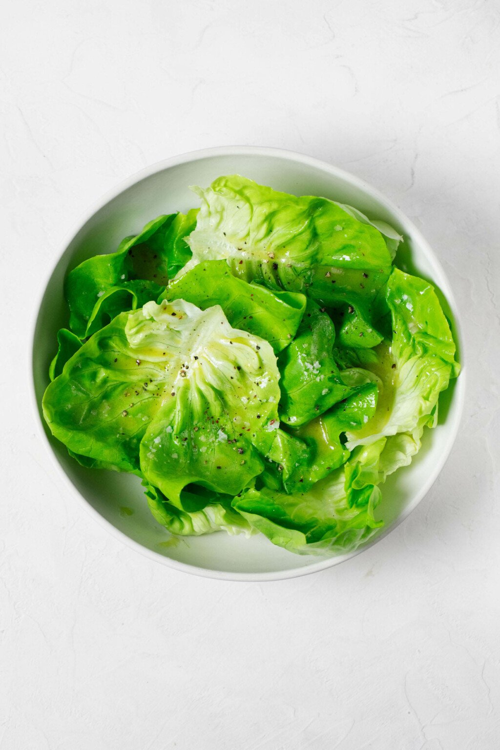 An overhead image of a round white bowl, which has been filled with a fresh green butter lettuce salad.
