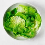 An overhead image of a round white bowl, which has been filled with a fresh green butter lettuce salad.