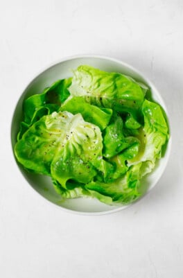 An overhead image of a round white bowl, which has been filled with a fresh green butter lettuce salad.