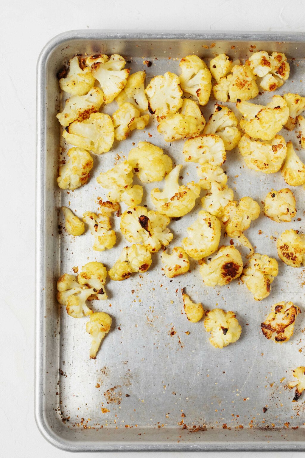 An overhead image of a silver colored oven baking sheet, which is topped with roasted cauliflower.
