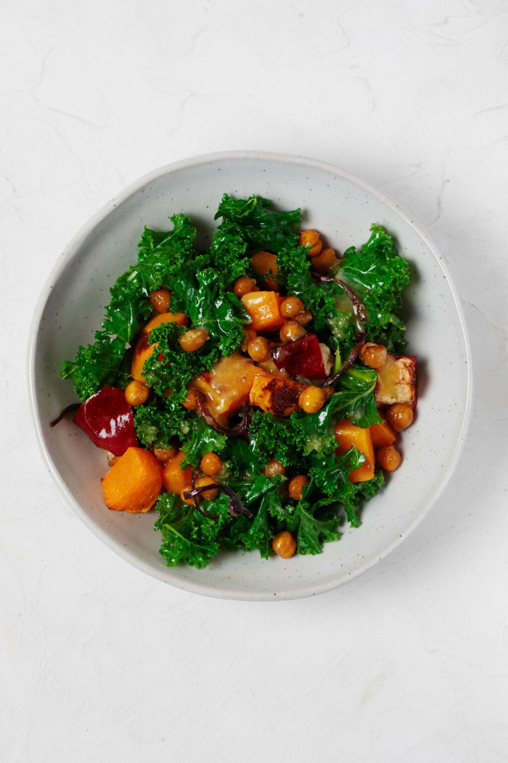 An overhead image of a white bowl, which is filled with kale, squash, and other ingredients.