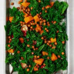 An overhead image of a metal sheet pan, which is covered in a festive kale saiad with roasted butternut squash and chickpeas.