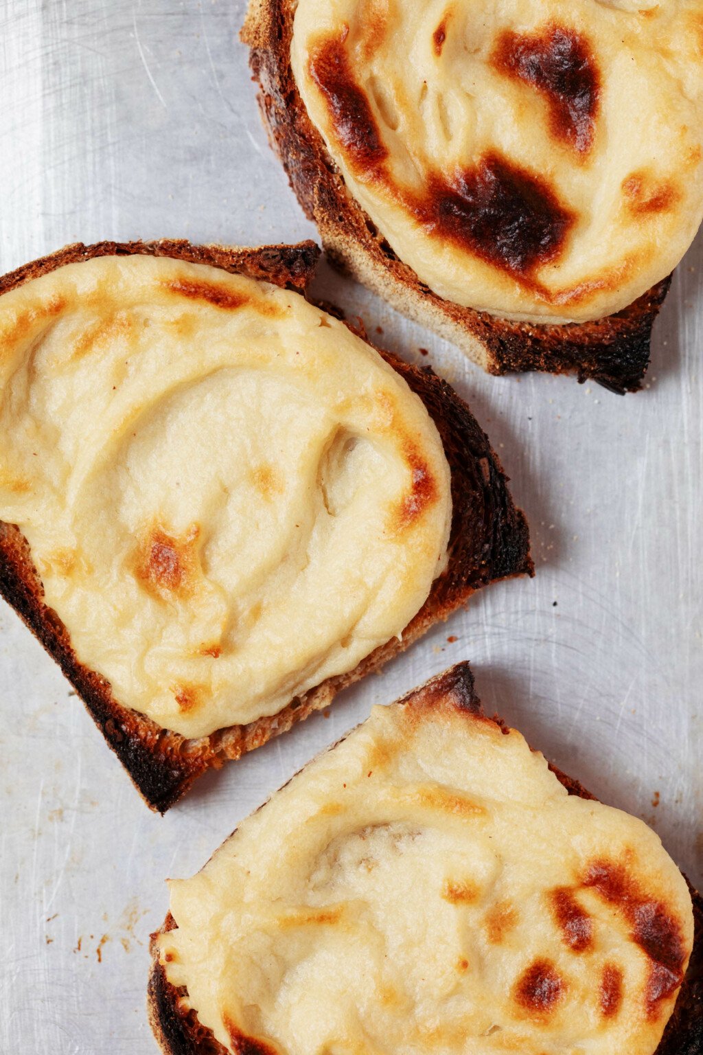 An overhead image of toasted bread with browned, plant-based cashew cheese on top.