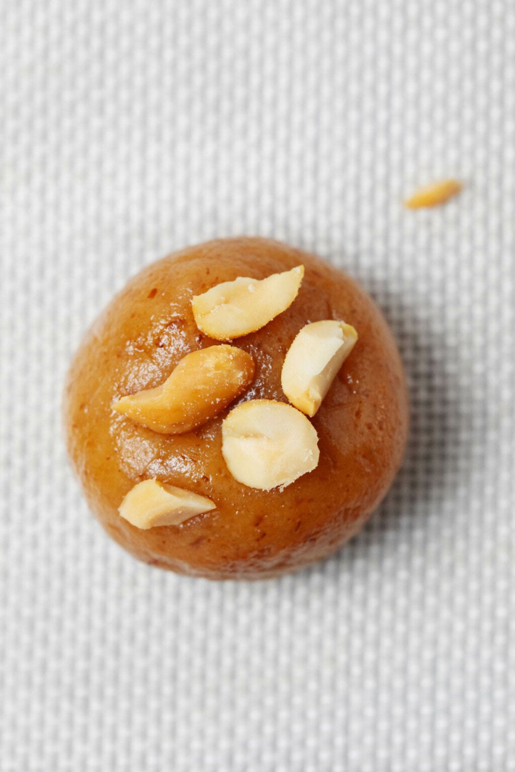 A close-up, overhead image of a round ball of cookie dough, topped with a few chopped pieces of peanut.