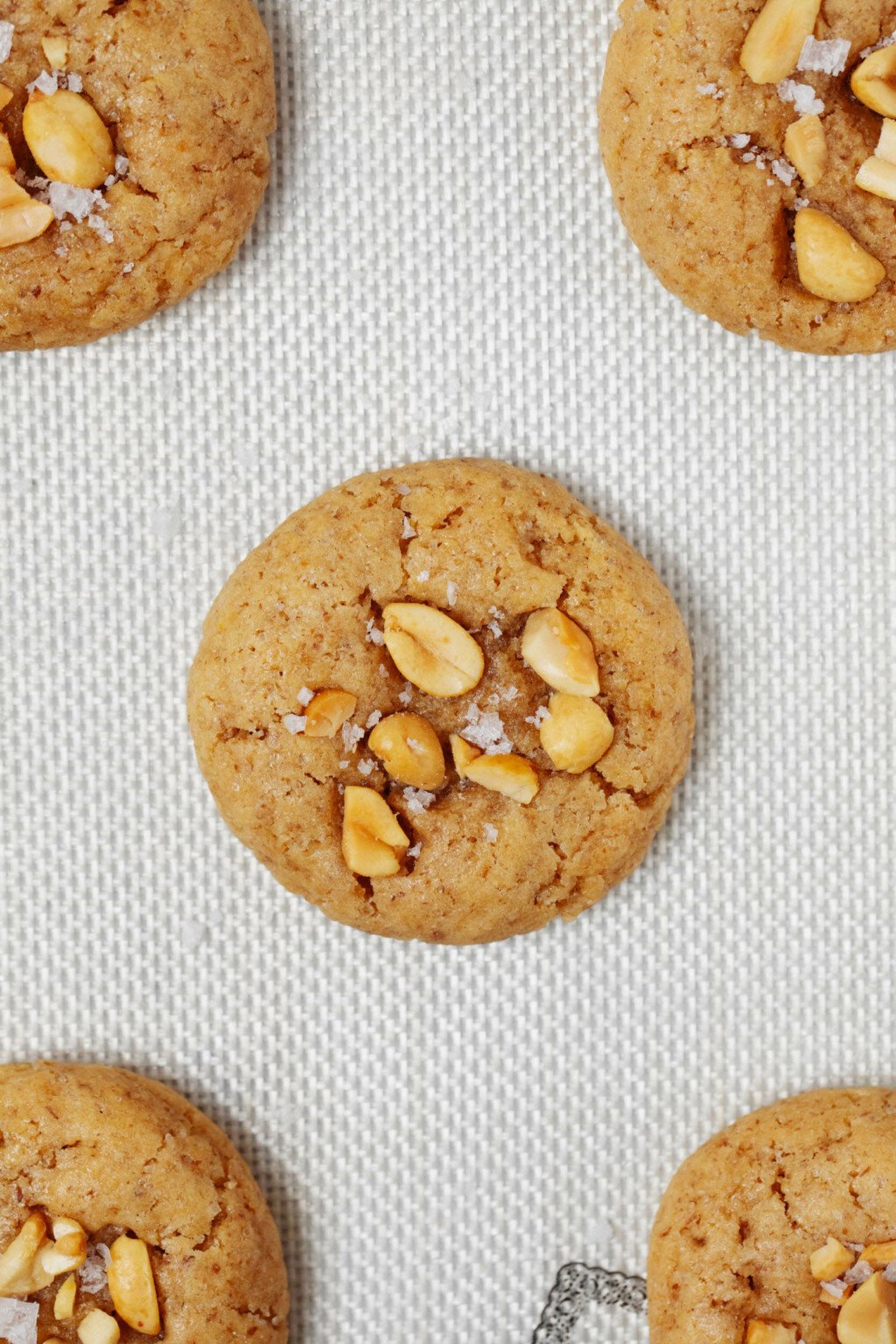 A light-colored, Silpat baking sheet is topped with round, puffy peanut cookies.