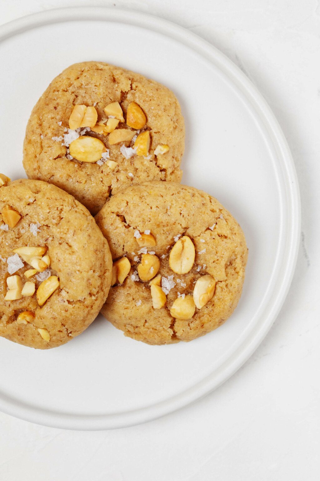 Three round, puffy vegan peanut cookies are positioned on a round, white plate.