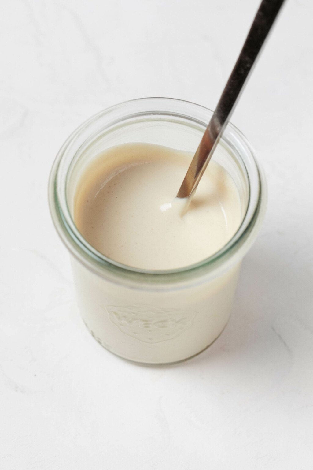 A Weck mason jar, resting on a white surface, holds a cream-colored tahini dressing.