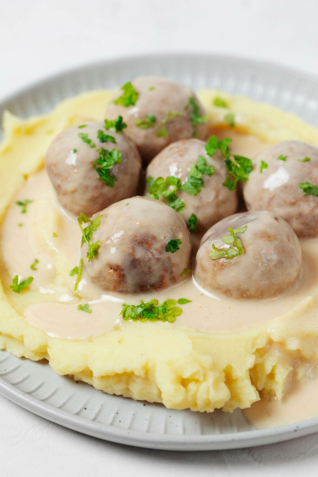 A close-up image of creamy mashed potatoes, which are topped with sauce and plant-based Swedish meatballs. 