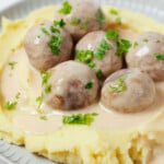 A close-up image of creamy mashed potatoes, which are topped with sauce and plant-based Swedish meatballs.