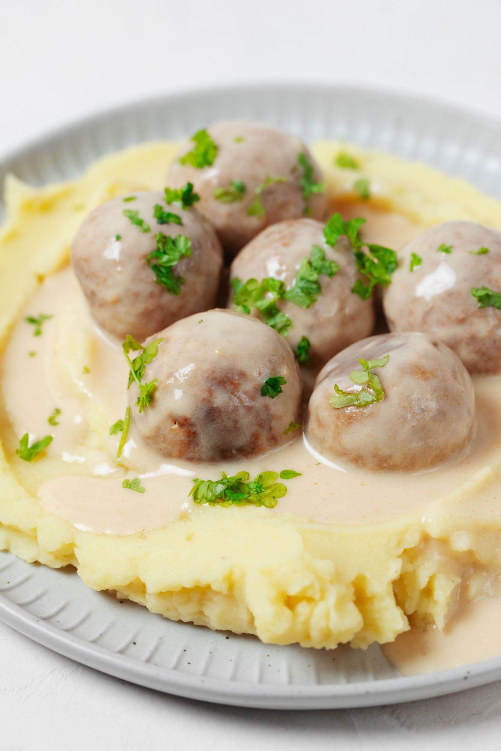 A close-up image of creamy mashed potatoes, which are topped with sauce and plant-based Swedish meatballs.