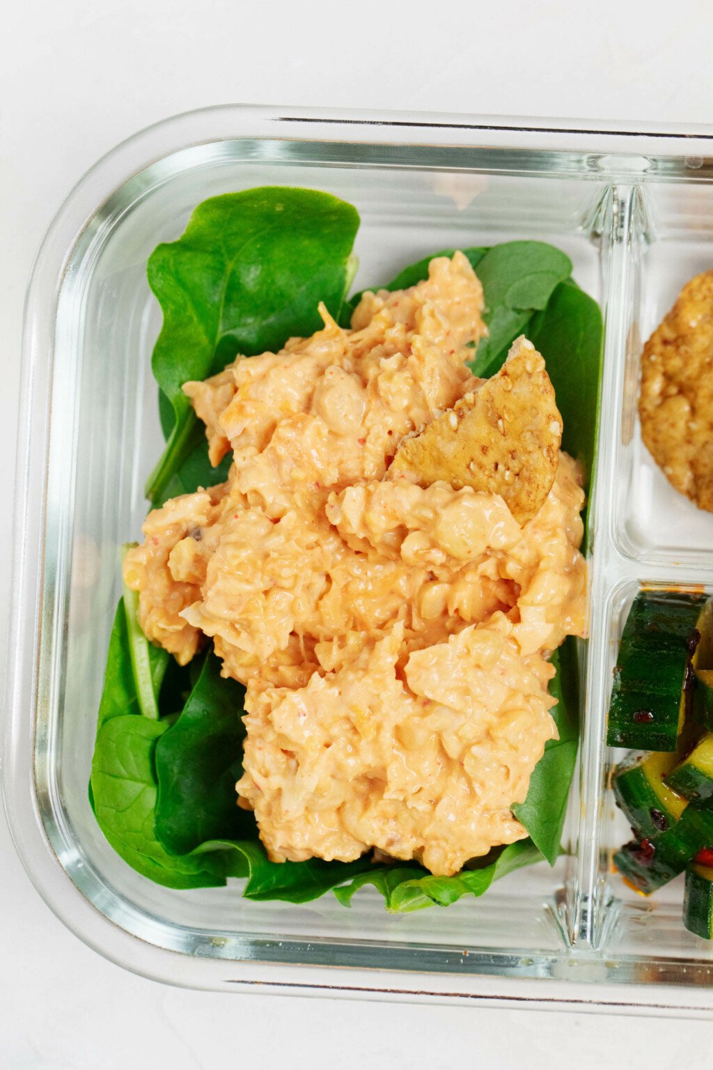 An overhead image of smashed chickpea salad with kimchi, which is served in a lunch box over greens.