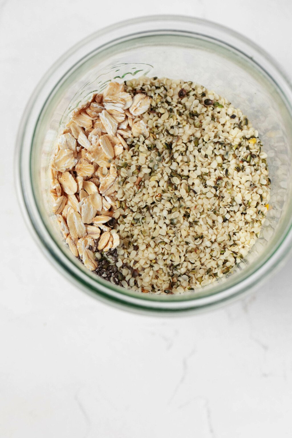 Chia seeds, rolled oats, and hemp seeds are visible in a glass mason jar, which rests on a white surface.
