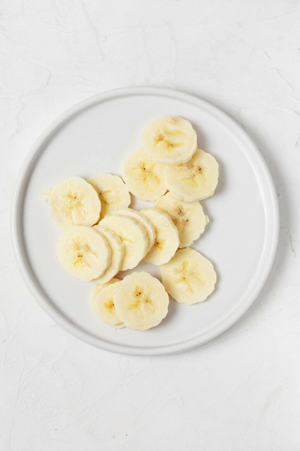 An overhead image of a small, round white plate, topped with banana slices.