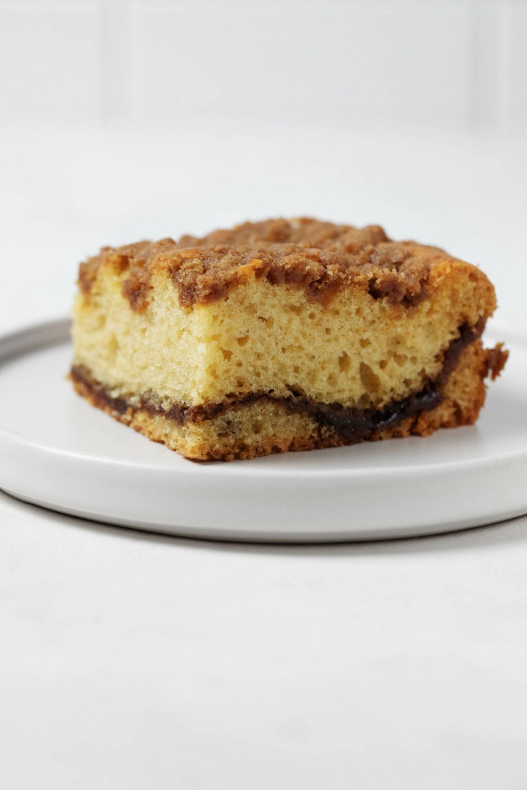 An angled photograph of a slice of vegan sour cream coffee cake, with a ribbon of cinnamon filling and streusel topping.
